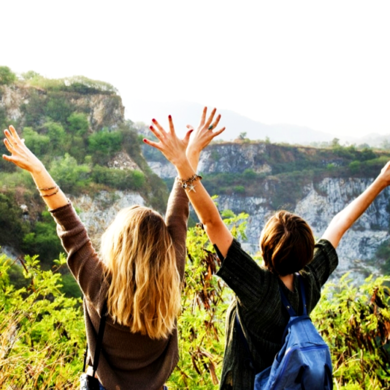 Two women in front of a mountain throwing their hands in the air
