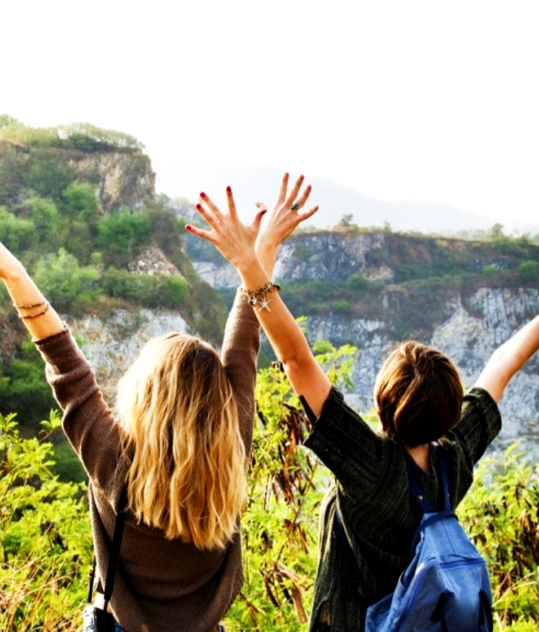 Two women in front of a mountain throwing their hands in the air