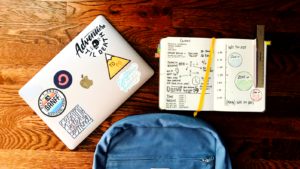 Flat lay photography of blue backpack beside book and silver MacBook
