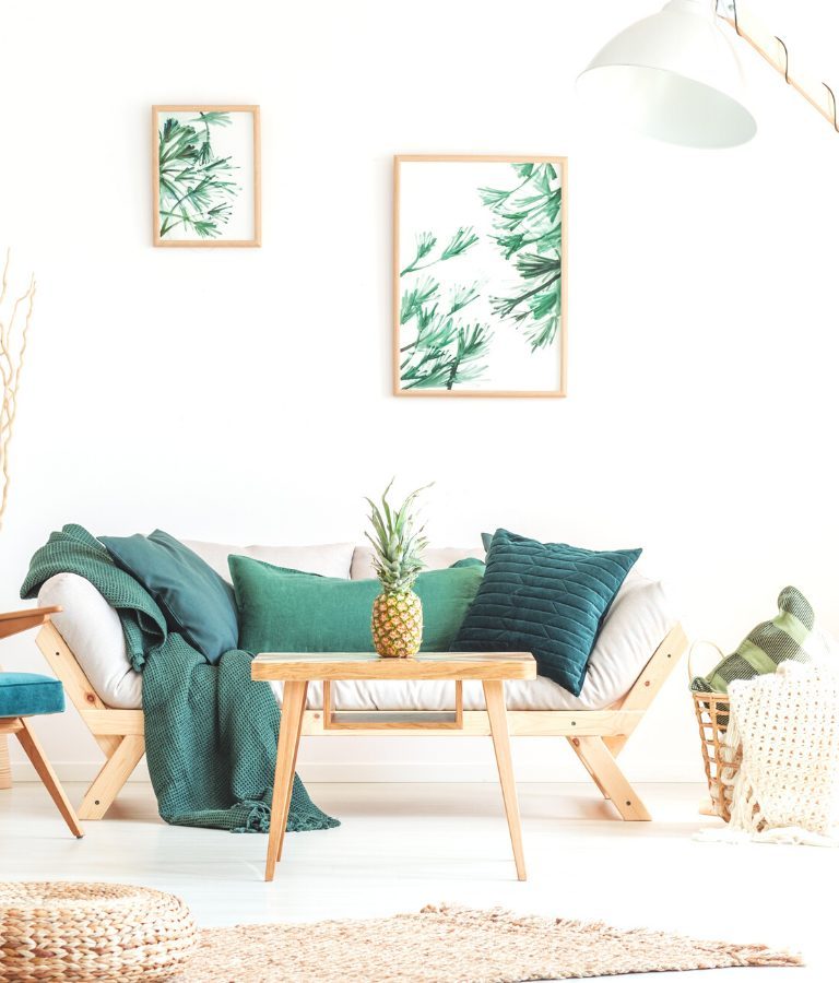Pineapple on wood stool in living room with green furniture and braided pouf on carpet